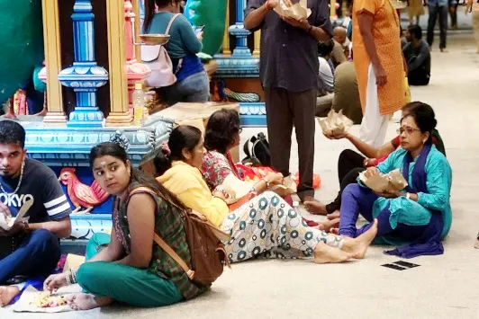 side the main temple, devotees are eating packaged vegetarian food sitting on the floor